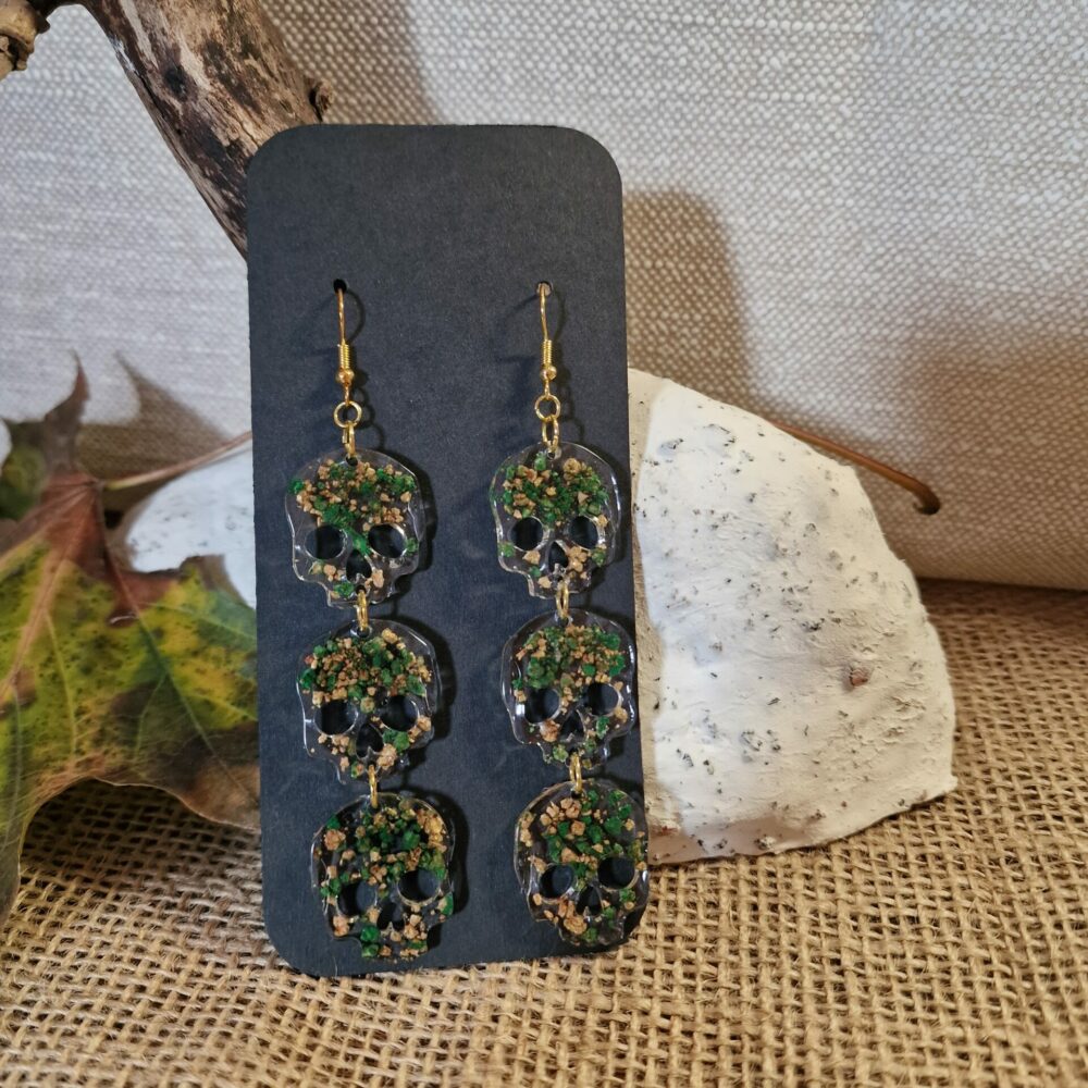 Boucles d’oreilles longues à têtes de mort vertes en résine transparente, avec inclusions de liège et éclats verts, attaches dorées – Cé’rénité.