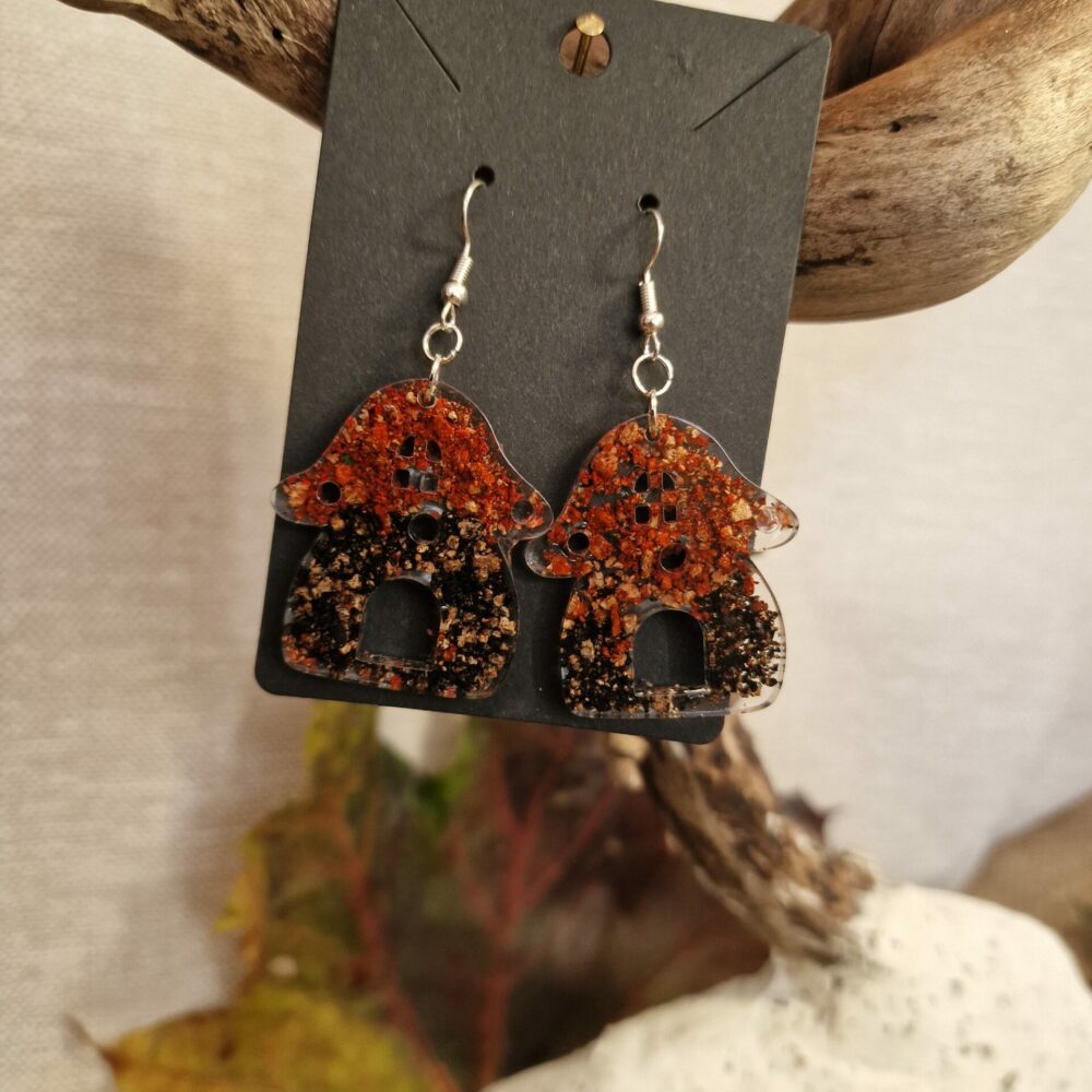 Boucles d’oreilles artisanales Cé’rénité en forme de champignons, réalisées en résine transparente avec inclusions de liège et éclats colorés rouges, noirs et naturels, attaches argentées.