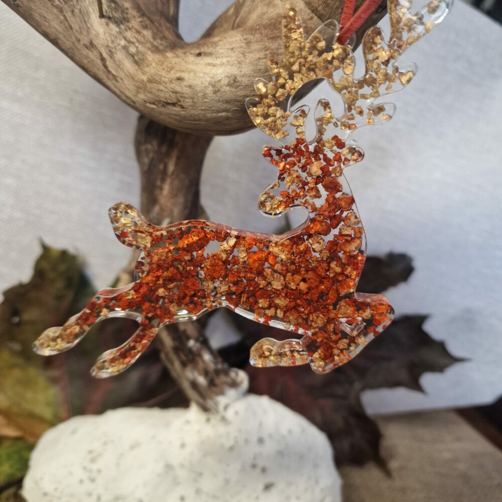 Décoration artisanale Cé’rénité représentant un renne rouge cuivré aux reflets dorés, réalisée en résine transparente avec éclats de liège recyclé et cordon en suédine, 15 x 10 cm.