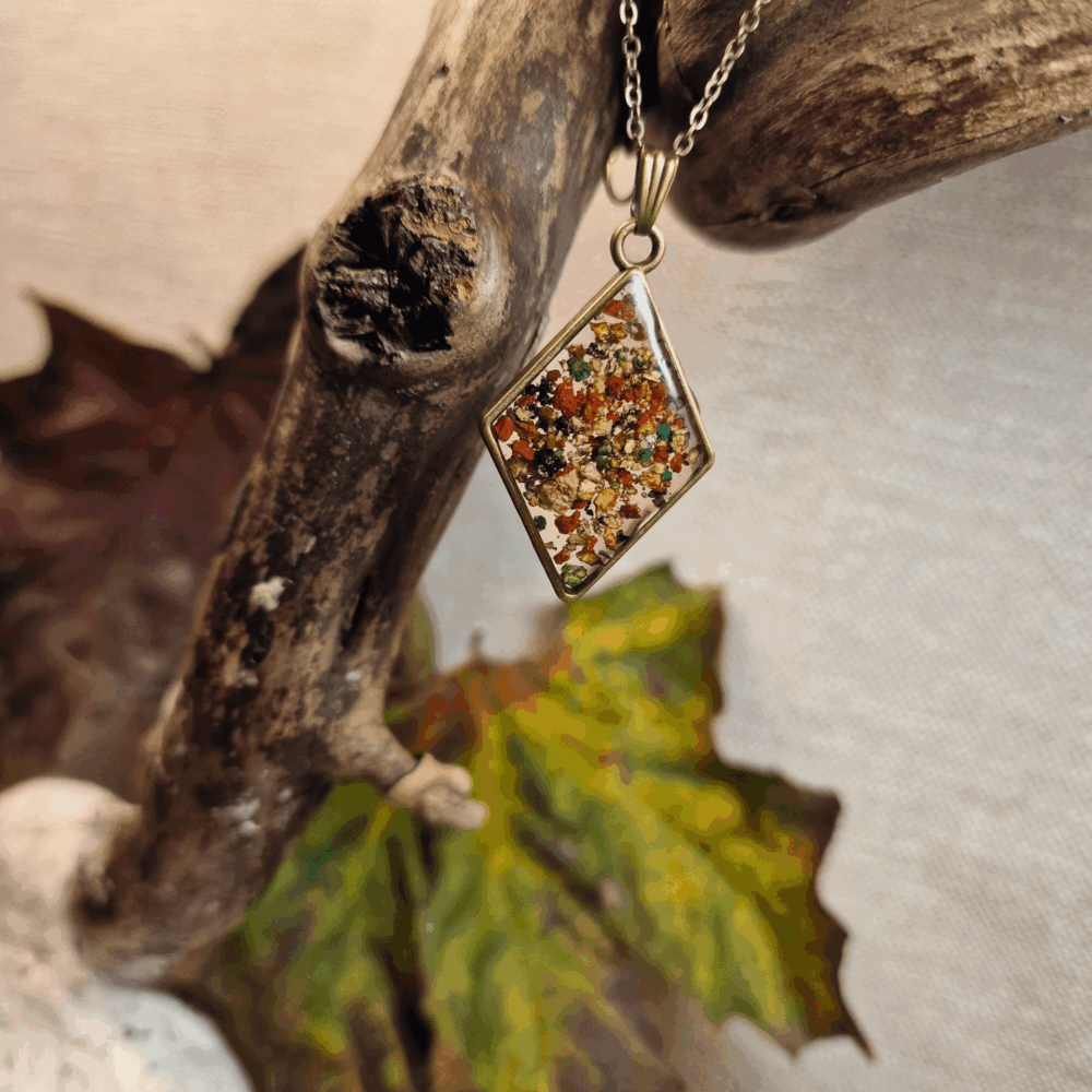 Collier artisanal Cé’rénité en résine transparente et liège naturel avec éclats rouges et verts, pendentif losange bronze sur chaîne assortie.
