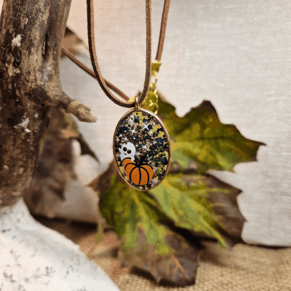 Collier ovale en résine avec éclats verts, bleus et dorés, mini citrouille et fantôme, monté sur cordon en simili cuir brun avec apprêts dorés.