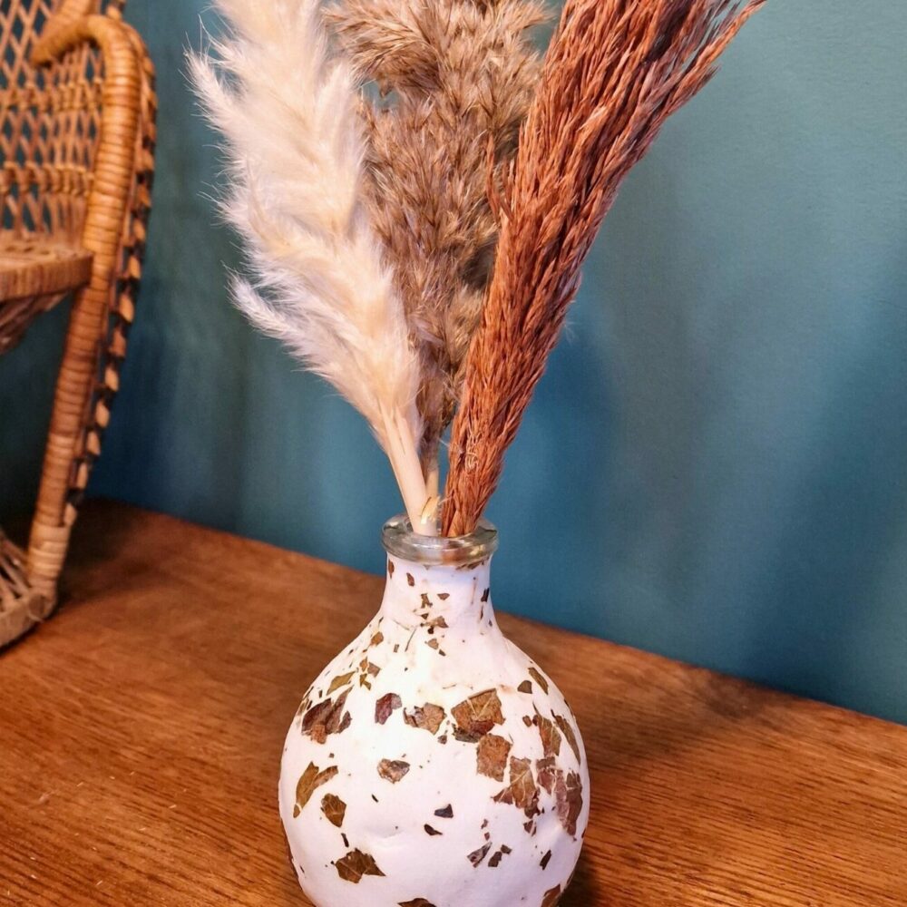 Vase artisanal en verre recyclé recouvert d’argile blanche avec feuilles naturelles incrustées.