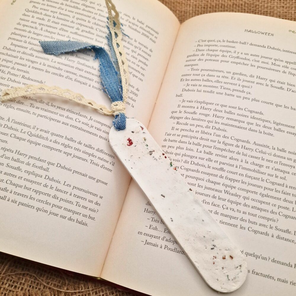 Marque-page artisanal en argile blanche avec éclats de liège de différentes couleurs, posé dans un livre ouvert, création Cé’rénité.